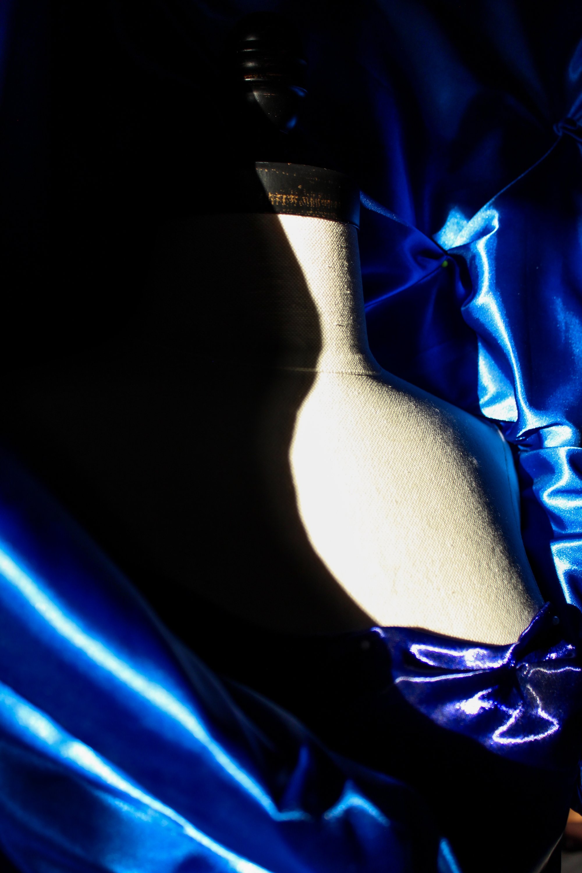 Royal blue satin draped against a dressform, lit from the side.